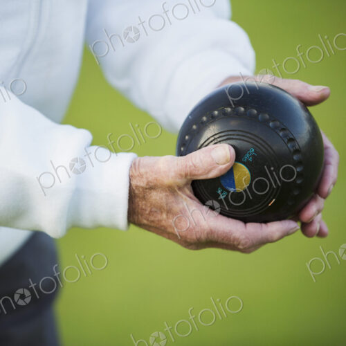 A man holding a black wooden lawn bowls ball in his hands. Notches and grooves in the… A man holding a black wooden lawn bowls ball in his hands. Notches and grooves in the…