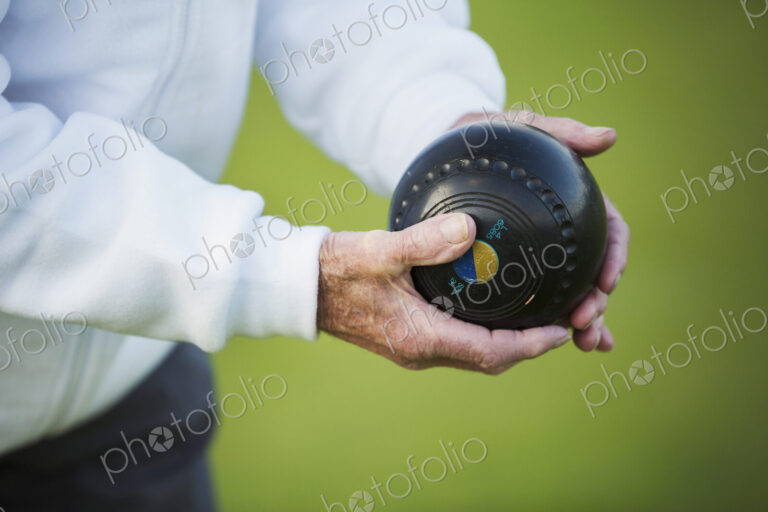A man holding a black wooden lawn bowls ball in his hands. Notches and grooves in the…
