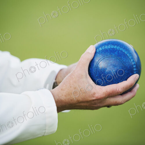 A man holding a blue wooden lawn bowls ball in his hands. A man holding a blue wooden lawn bowls ball in his hands.
