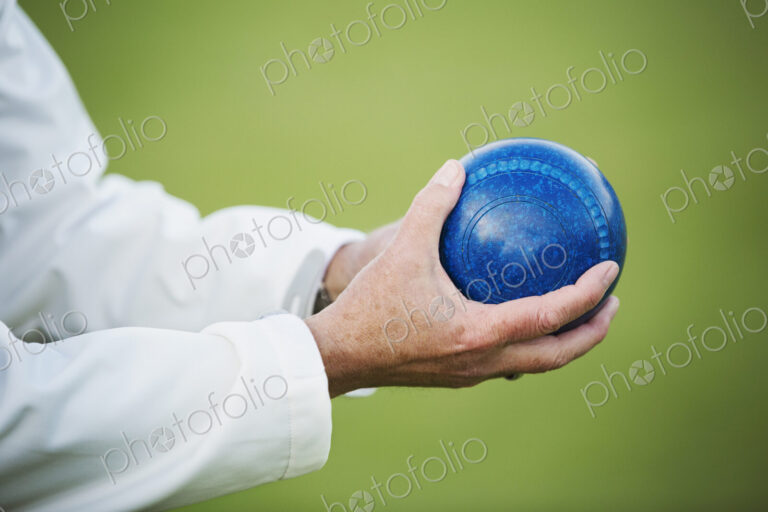 A man holding a blue wooden lawn bowls ball in his hands.