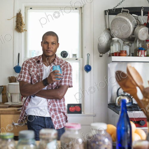 A man holding a drink standing in a farmhouse kitchen.