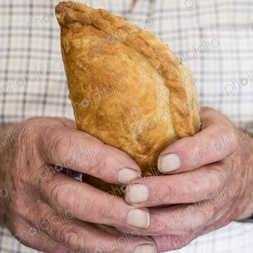 A man holding a fresh homemade pasty with a crimped edge, a regional speciality A man holding a fresh homemade pasty with a crimped edge, a regional speciality
