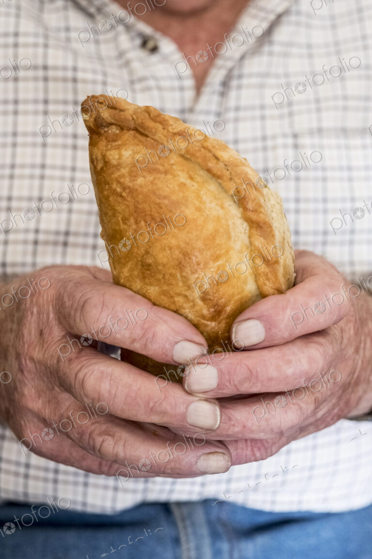 A man holding a fresh homemade pasty with a crimped edge, a regional speciality