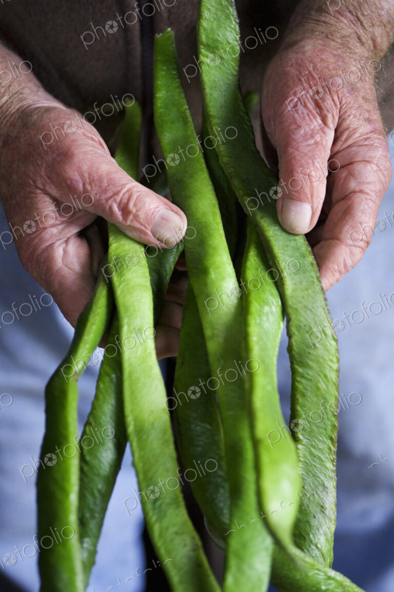 A man holding a handfull of long vivid green runner beans, fresh vegetables.
