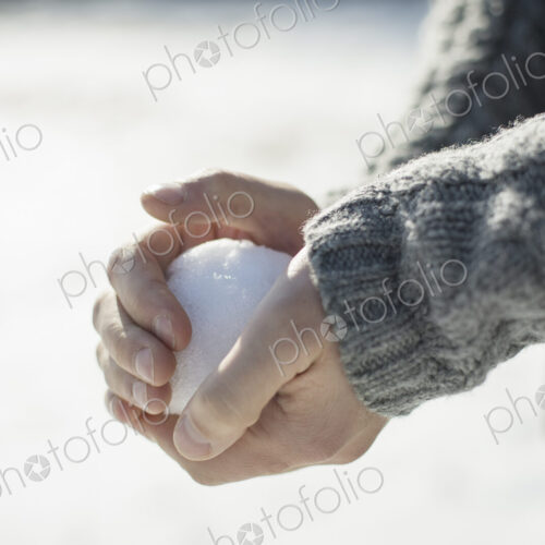 A man holding a large snowball in his bare hands. A man holding a large snowball in his bare hands.