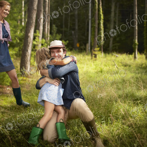 A man hugging a young child. A family on a woodland walk. A man hugging a young child. A family on a woodland walk.