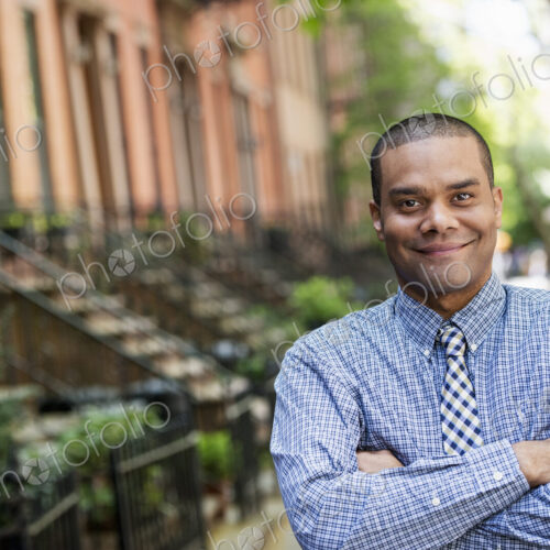 A man in a blue shirt and tie standing on a city street. A terrace of townhouses. A man in a blue shirt and tie standing on a city street. A terrace of townhouses.