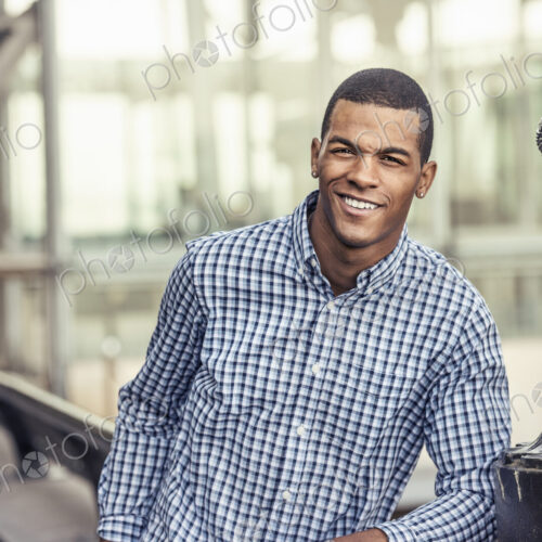 A man in a blue shirt leaning on a railing in a city park