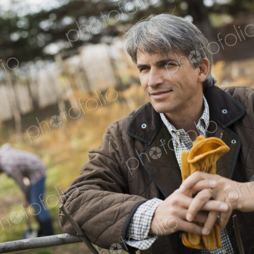 A man in a brown jacket, holding leather work gloves on an organic farm. A person… A man in a brown jacket, holding leather work gloves on an organic farm. A person…