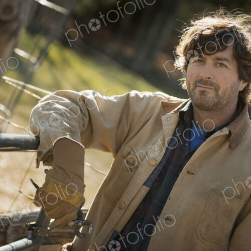 A man in a brown jacket, wearing work gloves leaning on a fence. Working on an organic… A man in a brown jacket, wearing work gloves leaning on a fence. Working on an organic…