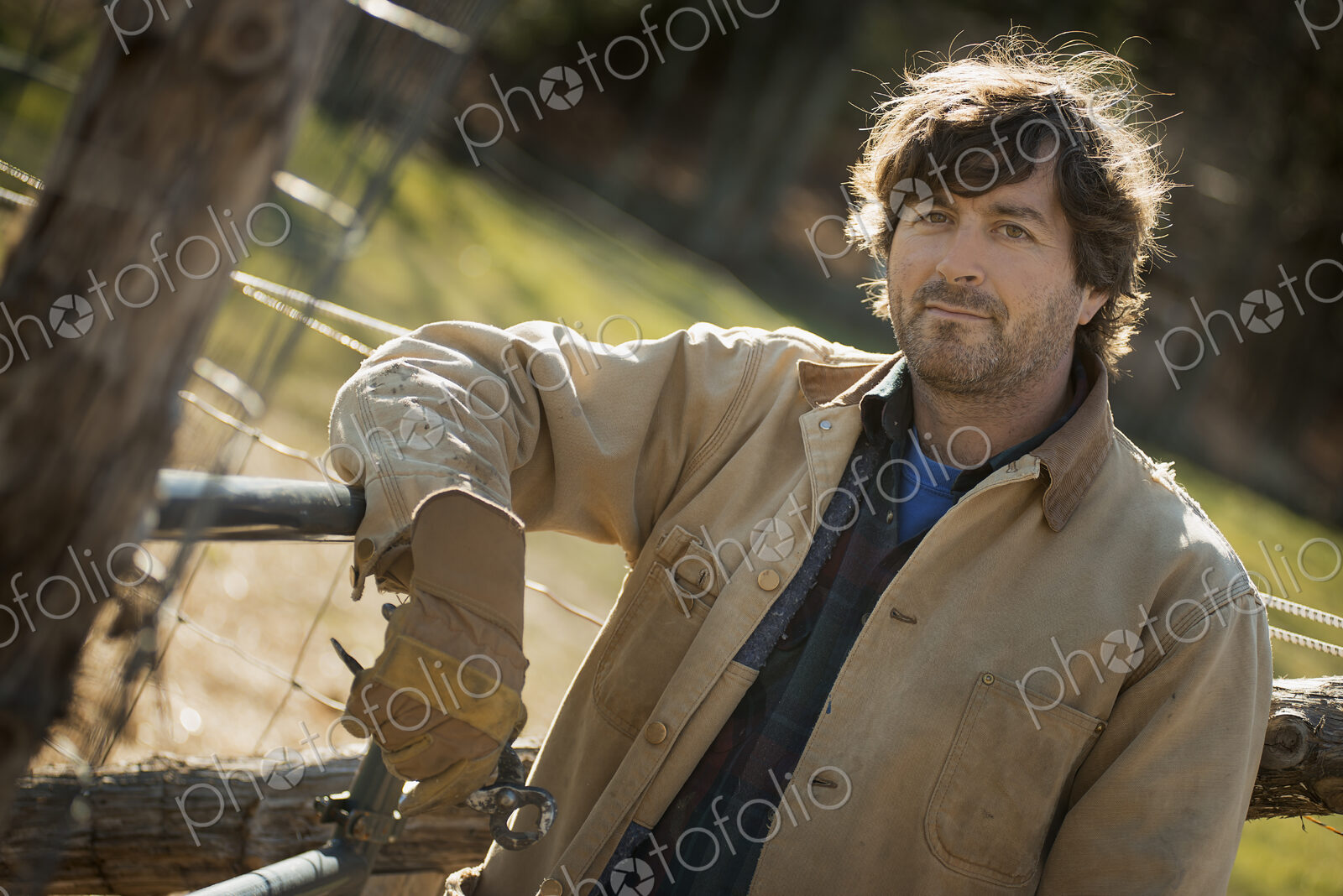 A man in a brown jacket, wearing work gloves leaning on a fence. Working on an organic…