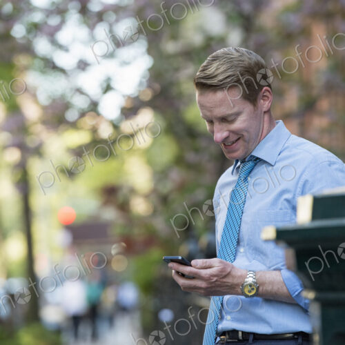 A man in a business shirt and tie outdoors in a city park. Looking down and checking… A man in a business shirt and tie outdoors in a city park. Looking down and checking…
