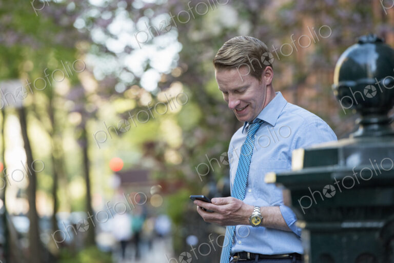 A man in a business shirt and tie outdoors in a city park. Looking down and checking…