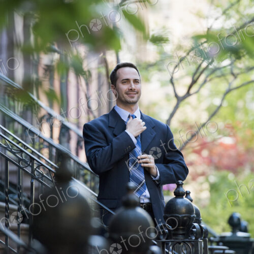 A man in a business suit adjusting his tie. At the bottom of the steps of a townhouse… A man in a business suit adjusting his tie. At the bottom of the steps of a townhouse…