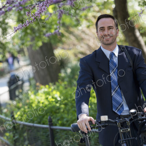 A man in a business suit astride a bicycle with helmet in hand. A man in a business suit astride a bicycle with helmet in hand.