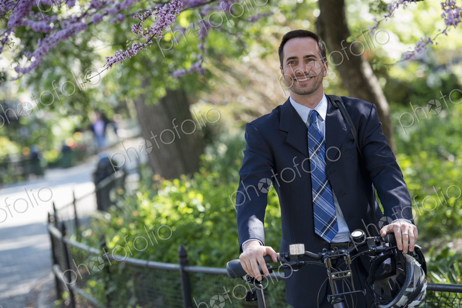 A man in a business suit astride a bicycle with helmet in hand.