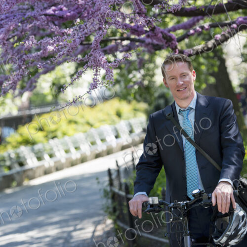 A man in a business suit, outdoors in a park. Sitting on a bicycle, with a cycle… A man in a business suit, outdoors in a park. Sitting on a bicycle, with a cycle…