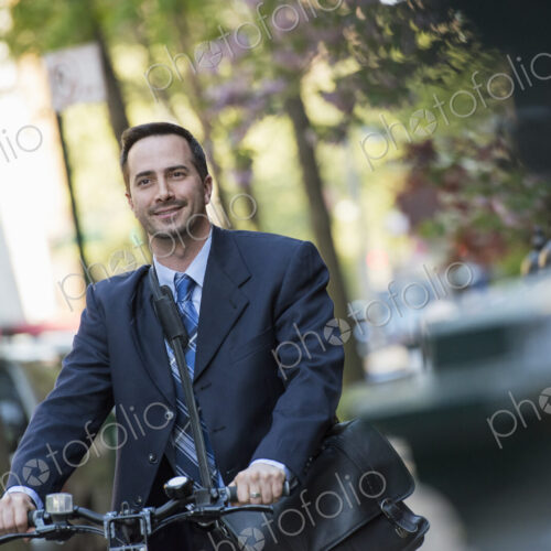 A man in a business suit, outdoors in a park. Sitting on a bicycle, with a cycle… A man in a business suit, outdoors in a park. Sitting on a bicycle, with a cycle…