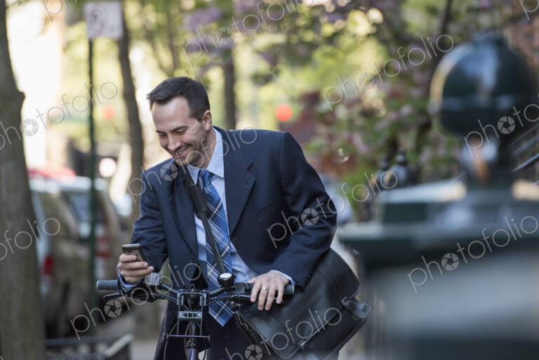 A man in a business suit, outdoors in a park. Sitting on a bicycle, with a cycle…