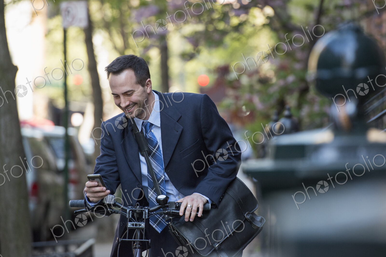 A man in a business suit, outdoors in a park. Sitting on a bicycle, with a cycle…