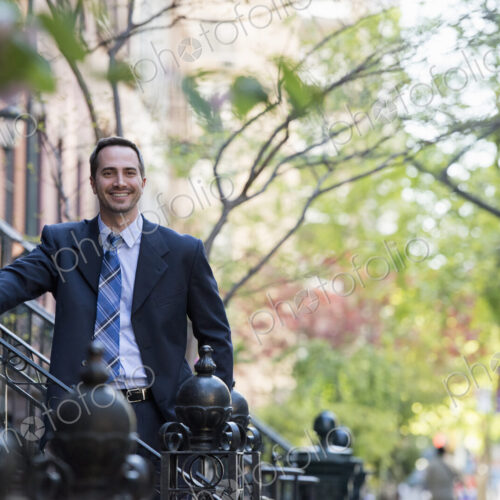 A man in a business suit standing on the steps in front of a row of residential… A man in a business suit standing on the steps in front of a row of residential…