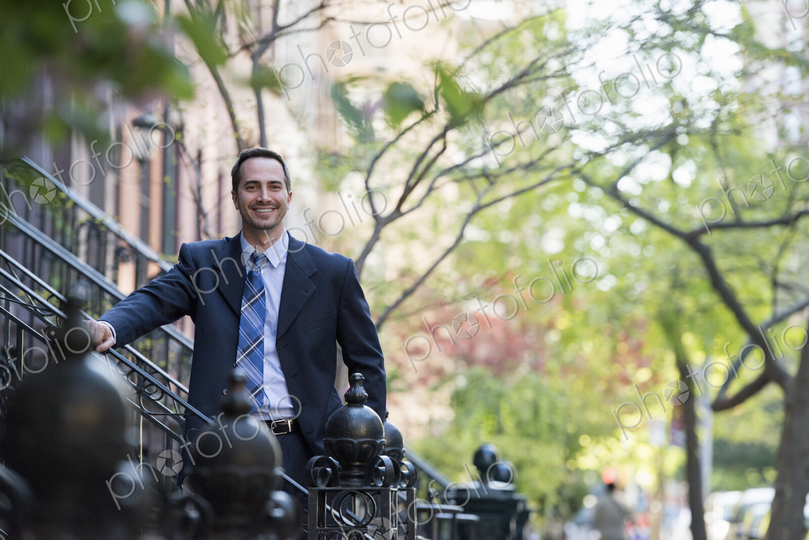 A man in a business suit standing on the steps in front of a row of residential…