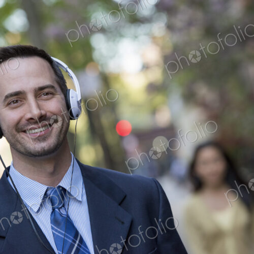 A man in a business suit wearing white headphones, listening music on the street. A… A man in a business suit wearing white headphones, listening music on the street. A…