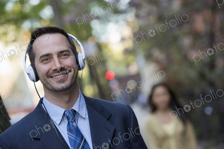 A man in a business suit wearing white headphones, listening music on the street. A…
