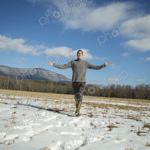 A man in a cable knit jumper and muck boots standing with his arms stretched out, in a… A man in a cable knit jumper and muck boots standing with his arms stretched out, in a…