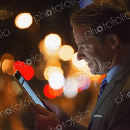 A man in a city at night, looking at a computer tablet.