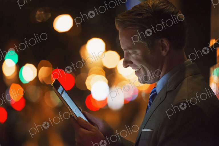 A man in a city at night, looking at a computer tablet.