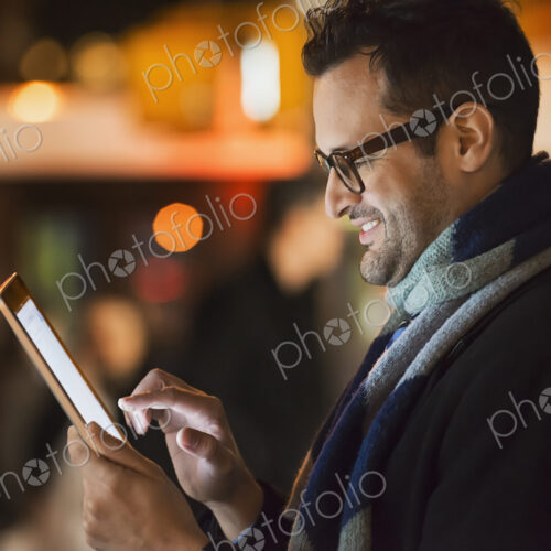 A man in a city at night, looking at a computer tablet.
