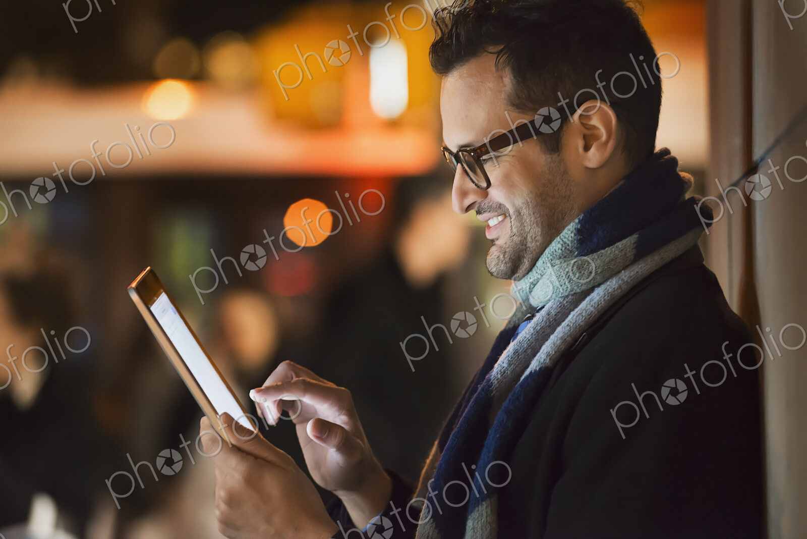 A man in a city at night, looking at a computer tablet.