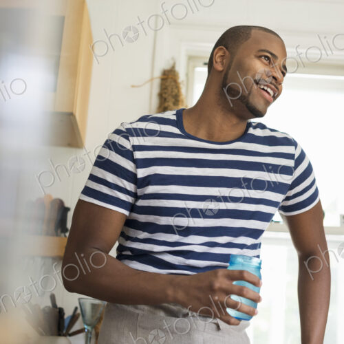 A man in a farmhouse kitchen holding a drink in a blue glass.