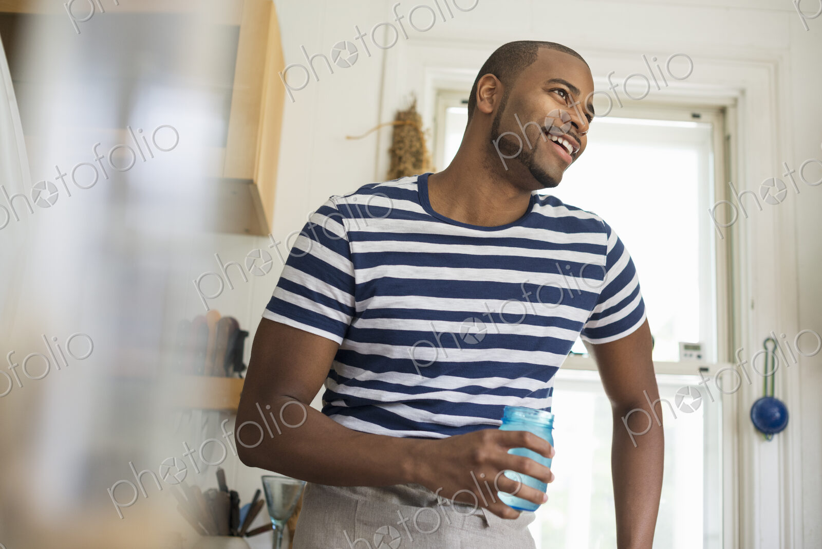 A man in a farmhouse kitchen holding a drink in a blue glass.