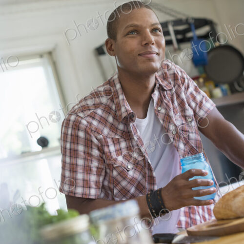 A man in a farmhouse kitchen with a glass in his hand. A loaf of bread. A man in a farmhouse kitchen with a glass in his hand. A loaf of bread.