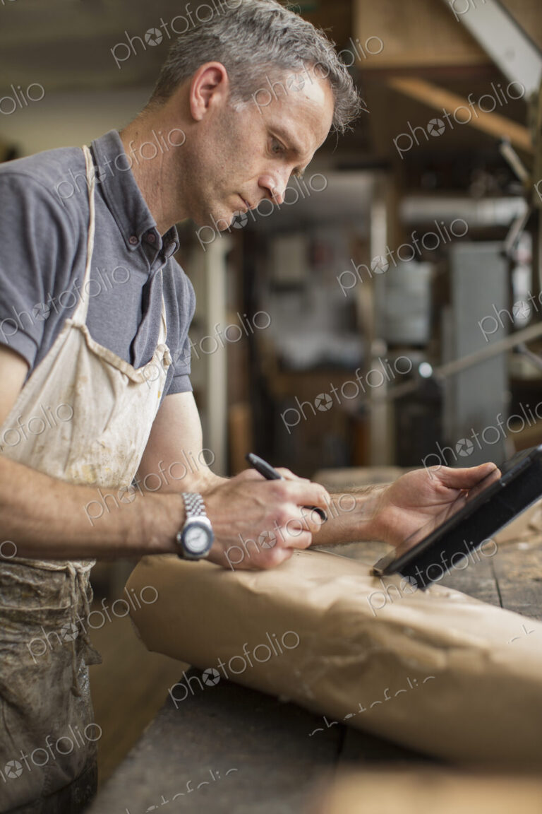 A man in a furniture restoration workshop using a digital tablet, writing on a packet…