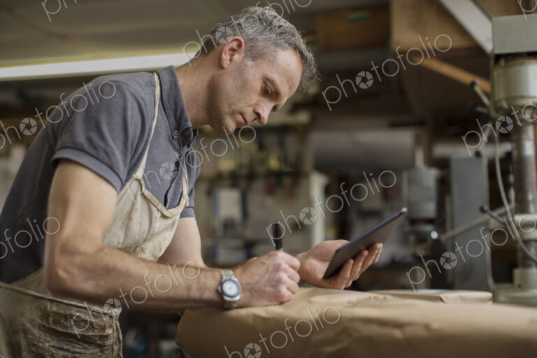 A man in a furniture restoration workshop using a digital tablet, writing on a packet…
