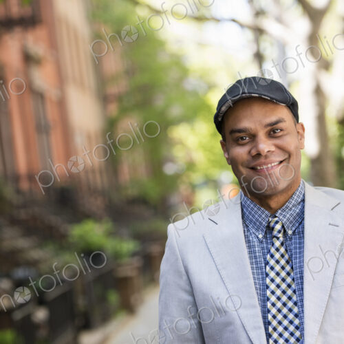 A man in a jacket and tie on a city street outside a terrace of brownstone houses. A man in a jacket and tie on a city street outside a terrace of brownstone houses.