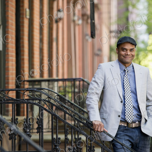 A man in a jacket and tie on a city street outside a terrace of brownstone houses. A man in a jacket and tie on a city street outside a terrace of brownstone houses.
