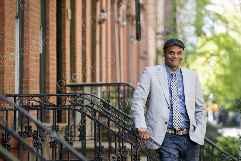 A man in a jacket and tie on a city street outside a terrace of brownstone houses.