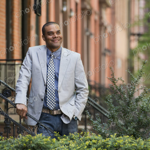 A man in a jacket and tie on a city street outside a terrace of brownstone houses. A man in a jacket and tie on a city street outside a terrace of brownstone houses.