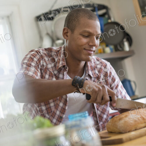 A man in a kitchen slicing a loaf of bread. A man in a kitchen slicing a loaf of bread.