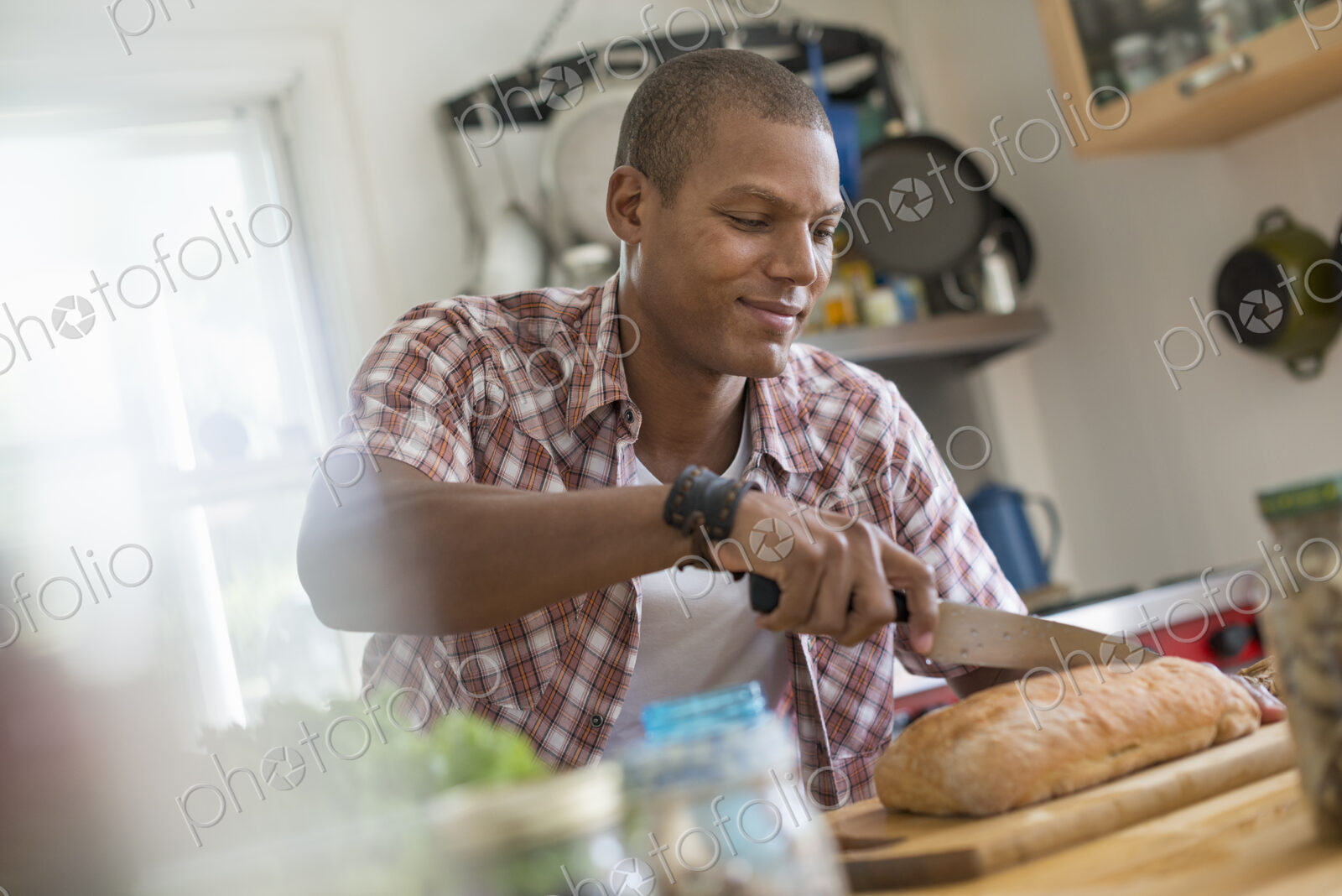 A man in a kitchen slicing a loaf of bread.