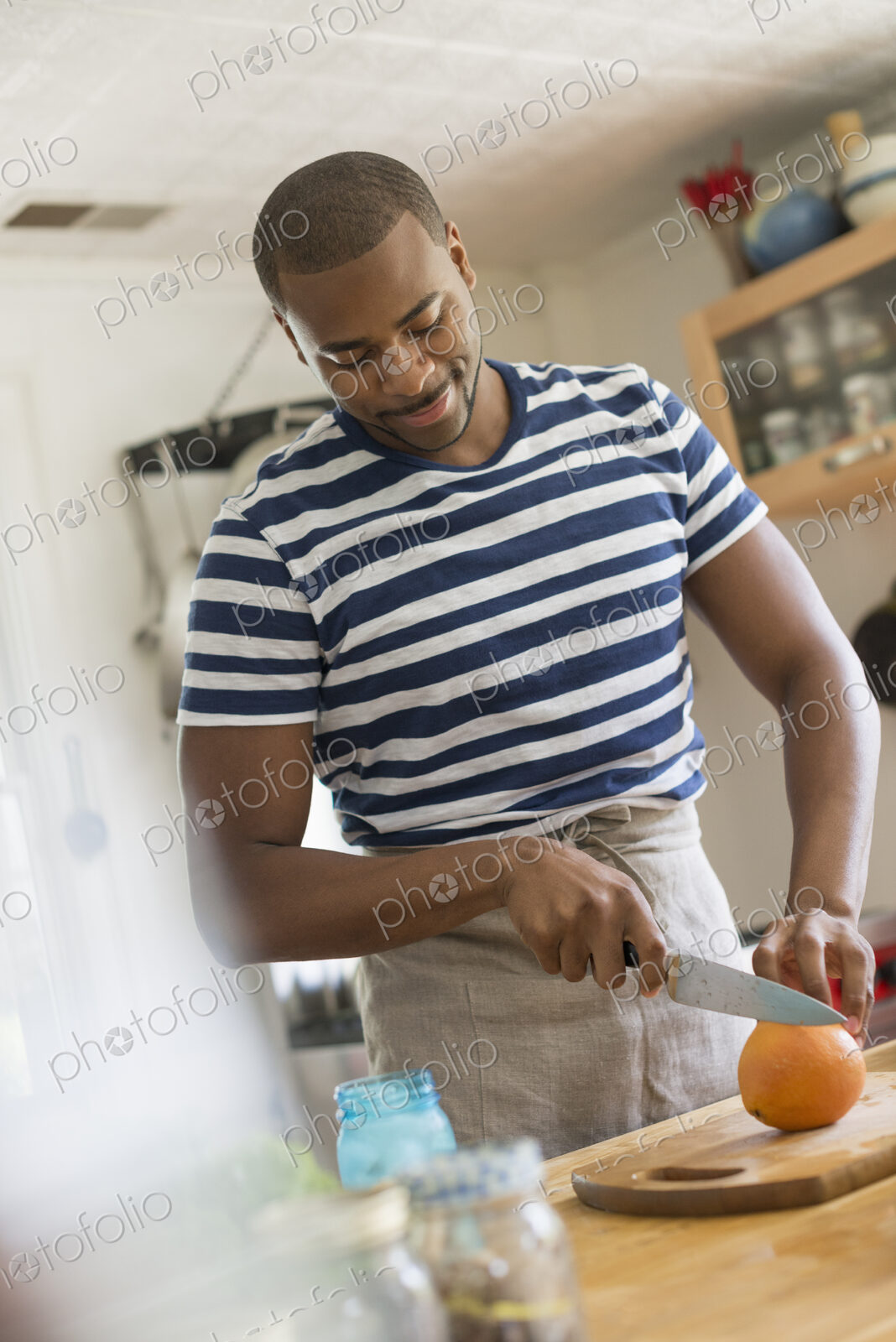 A man in a kitchen using a knife to slice an orange.