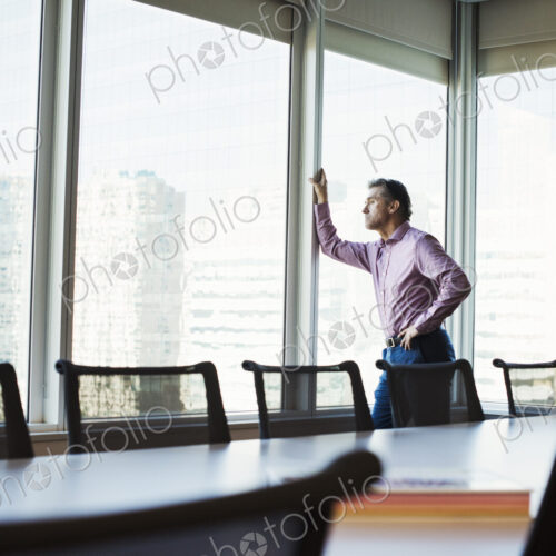 A man in a meeting room looking out of a window at an urban landscape.
