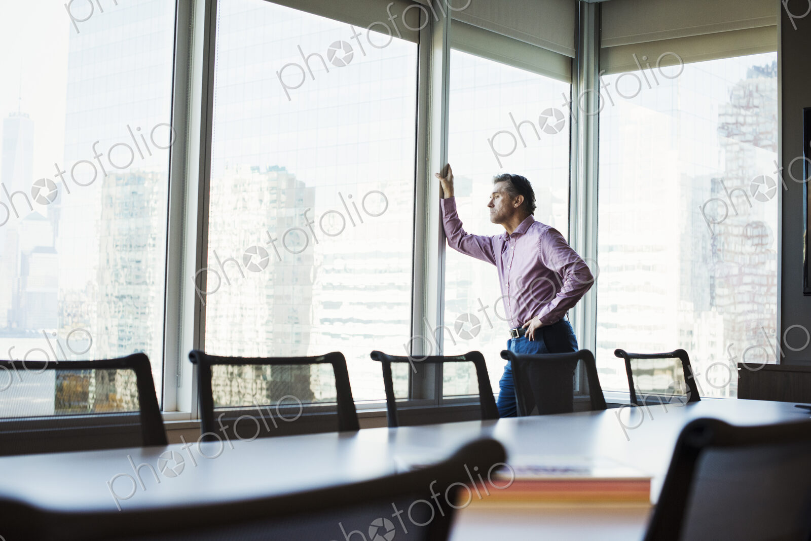 A man in a meeting room looking out of a window at an urban landscape.