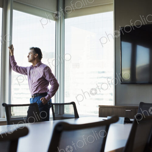 A man in a meeting room looking out of a window at an urban landscape.
