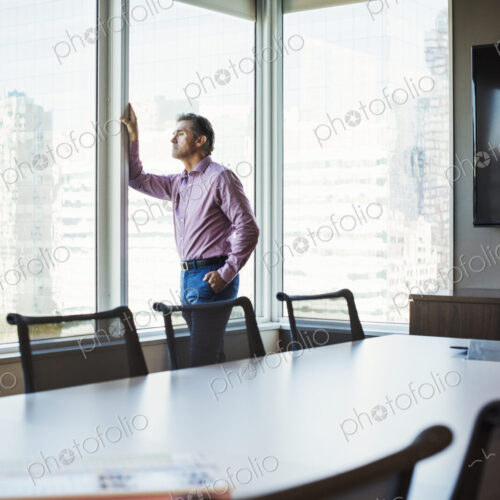A man in a meeting room looking out of a window at an urban landscape.