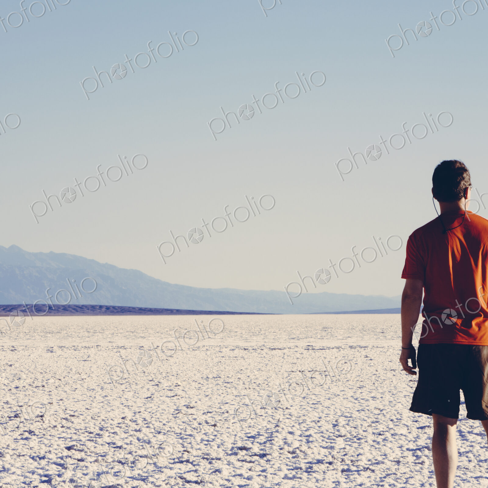 A man in a red shirt and shorts, standing on the salt flats overlooking the desert at…